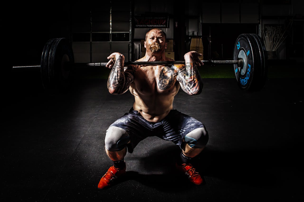 Home A tattooed man performing a heavy barbell squat in a gym for strength training.